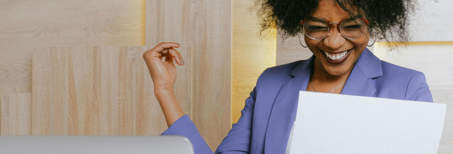 A cheerful woman celebrates her success at work, looking at a document in an office setting.