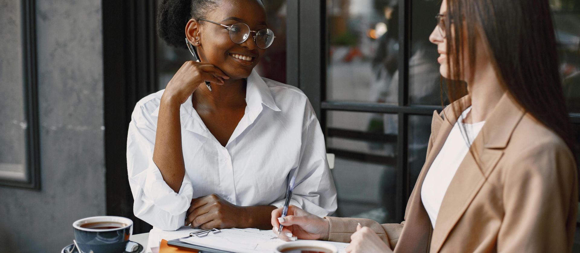 Two diverse women enjoying a business meeting at an outdoor cafe, discussing teamwork and cooperation.