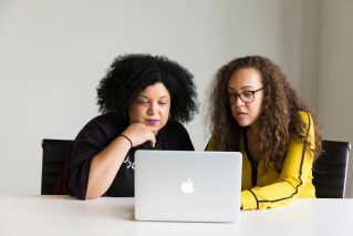 Two diverse women collaborating on a laptop in a modern office setting.